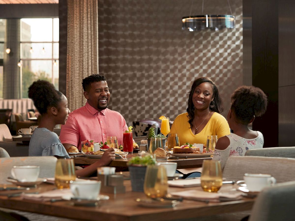 A group of four friends sits around a dining table enjoying a meal and conversation in a stylish, well-lit room.