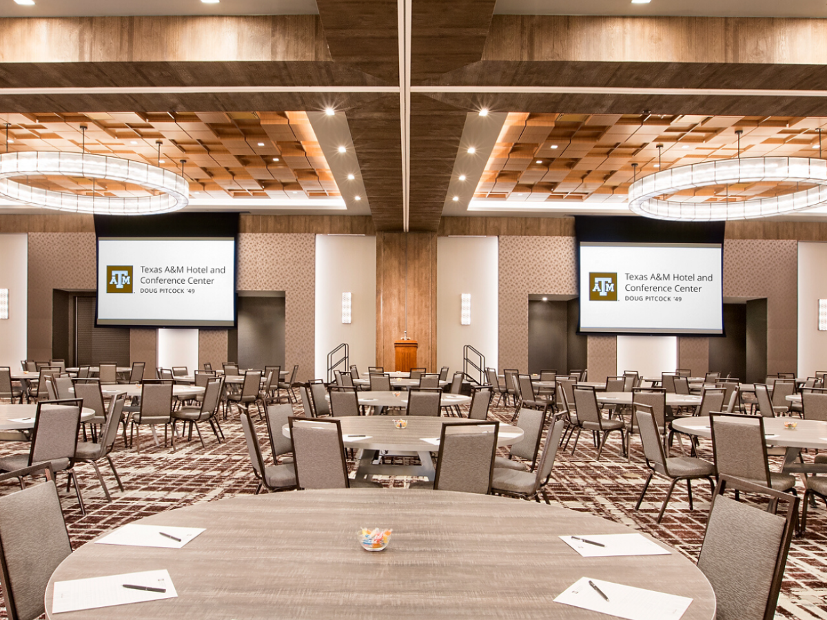 Century Ballroom organized in rounds with projecter slides lowered and Texas A&M Hotel notepads and pens