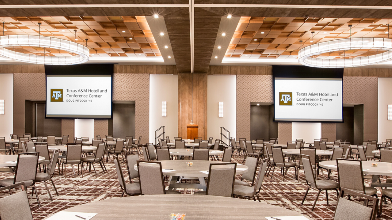 Century Ballroom organized in rounds with projecter slides lowered and Texas A&M Hotel notepads and pens