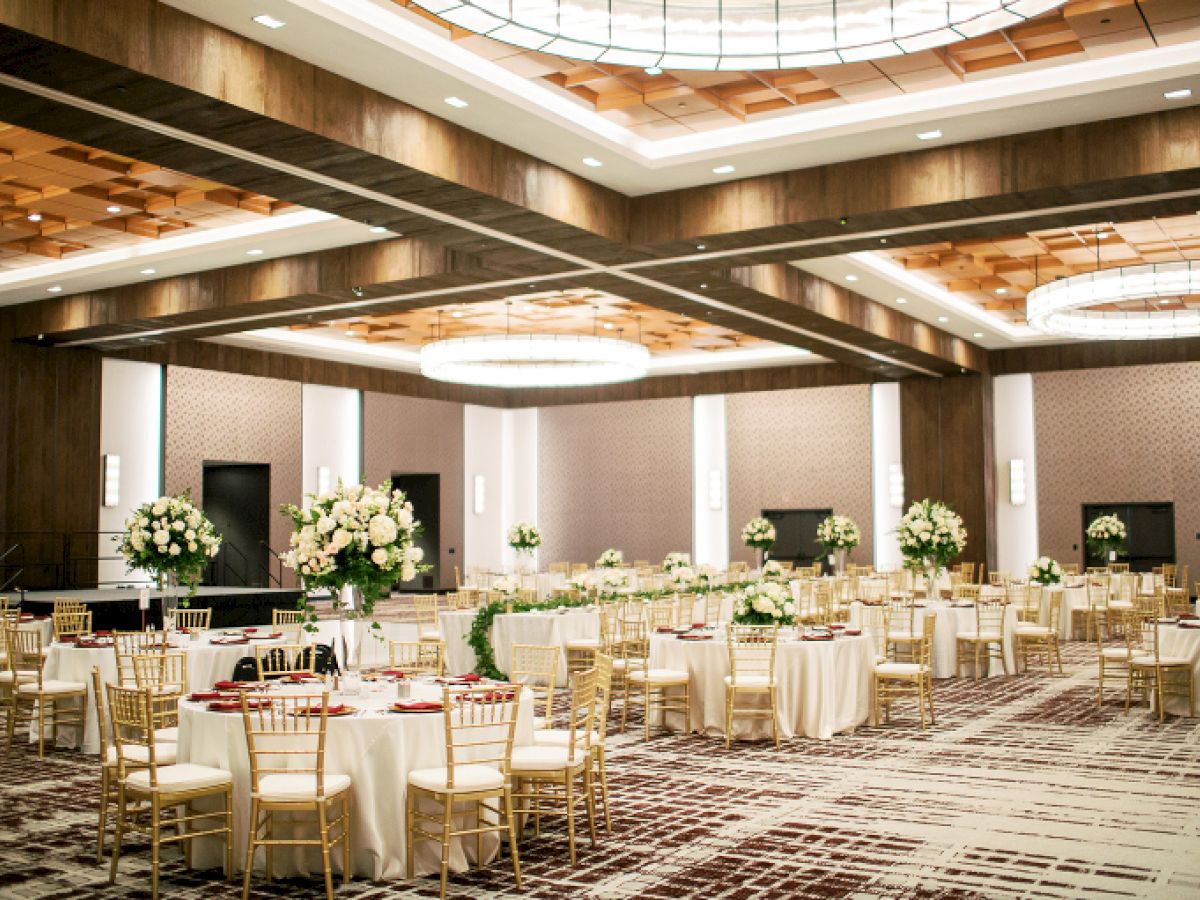 Century Ballroom set for a wedding reception featuring gold chairs. white table clothes, and large white floral arrangements