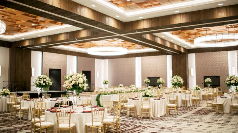 Century Ballroom set for a wedding reception featuring gold chairs. white table clothes, and large white floral arrangements
