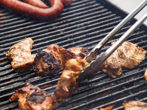 Grilling scene with sausages and marinated chunks of meat being turned with tongs on a barbecue grill.