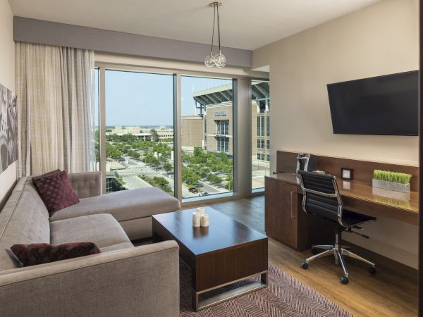 Corner suite entertainment area with a grey couch, mounted tv and work desk with a chair