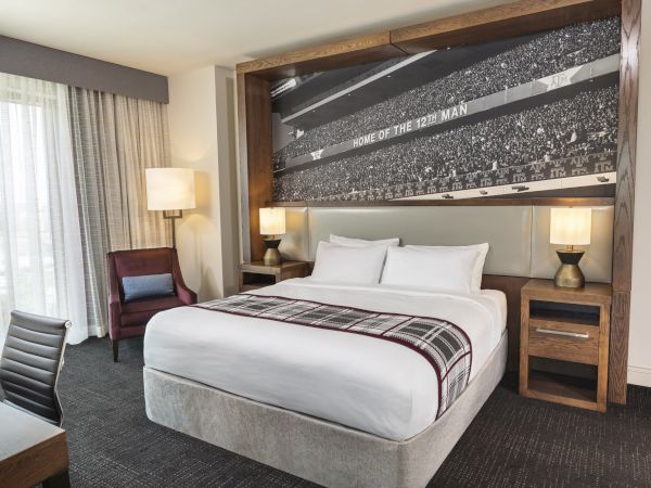 Modern corner suite hotel room featuring natural wood night stands, warm lighting, and a work desk and chair
