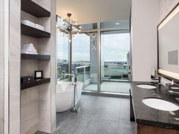 A modern bathroom with double vanity sinks, a freestanding bathtub, shelves with towels, and a large glass door opening to a balcony.