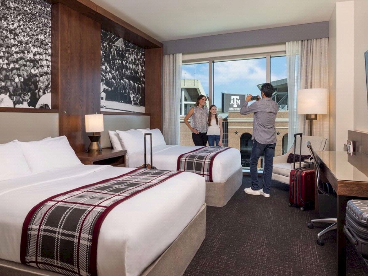 Father taking a photo of mother and daughter in a modern, double queen suite with a view of Kyle Field