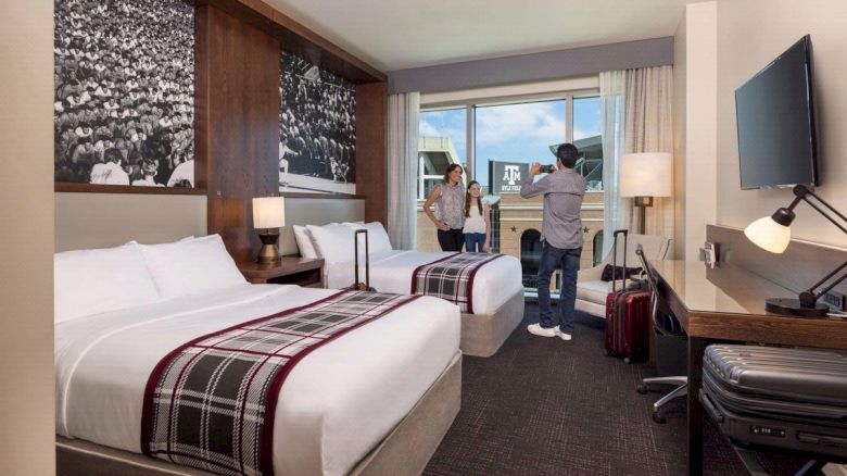 Father taking a photo of mother and daughter in a modern, double queen suite with a view of Kyle Field