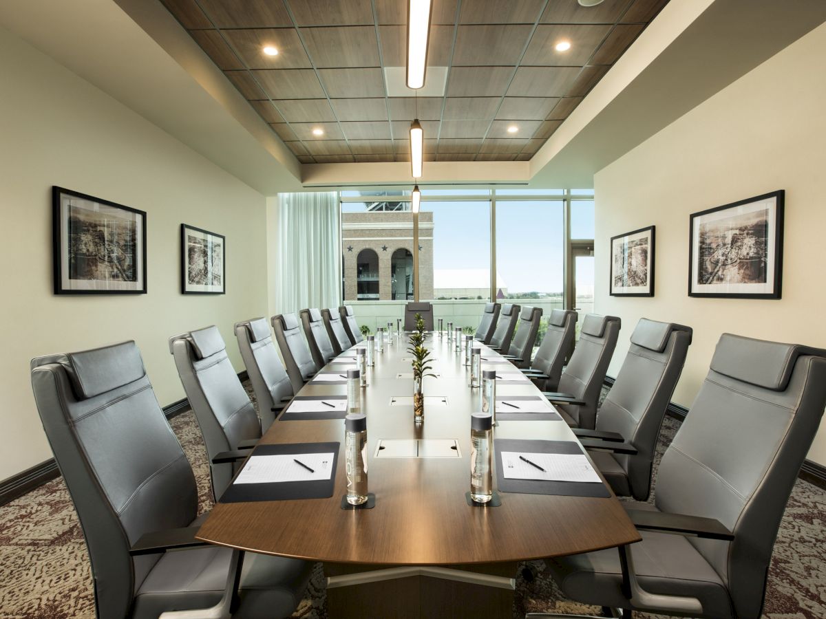 A modern conference room with a long table, twelve chairs, bottled water, notepads, and framed artwork on the walls.