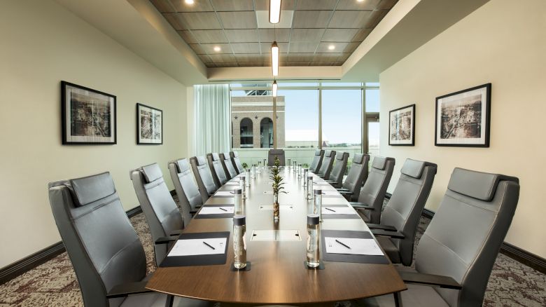 A modern conference room with a long table, twelve chairs, bottled water, notepads, and framed artwork on the walls.