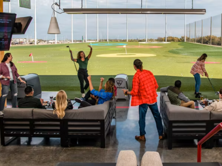 People are enjoying a game of golf at an indoor driving range with comfortable seating and relaxed atmosphere.