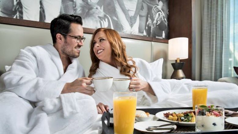 Couple enjoying breakfast in bed wearing robes and drinking coffee with a vintage photo in the background