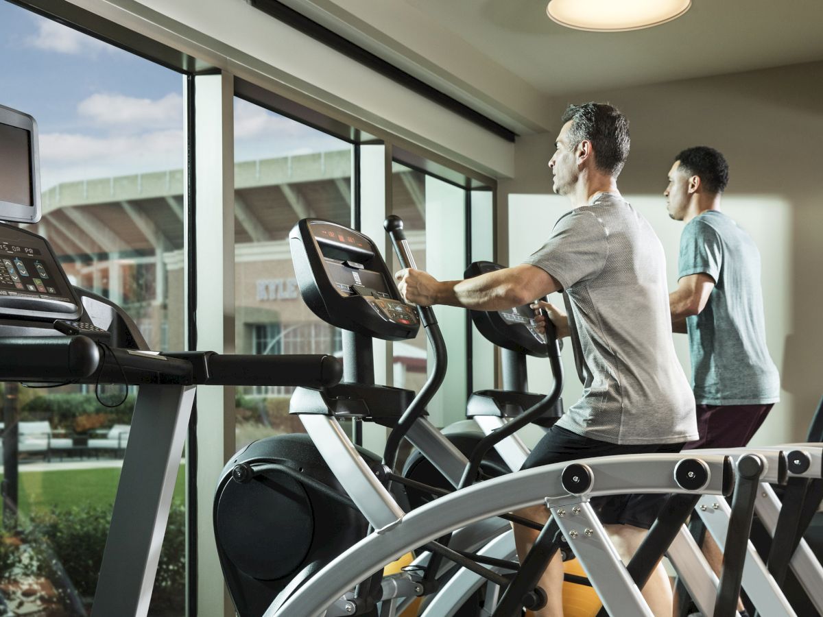 Two men running on elliptical machines in the gym overlooking Kyle Field