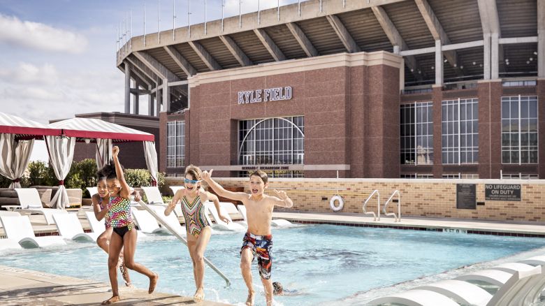 Kids running up the stairs of the rooftop pool with a view of Kyle Field in the background