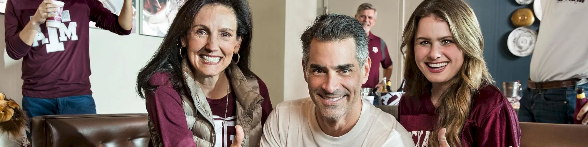 A group of smiling people wearing matching maroon and white attire, giving thumbs up, likely supporting a sports team.