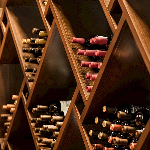 The image shows a wine rack with bottles of wine, arranged horizontally, and separated in diamond-shaped wooden compartments.