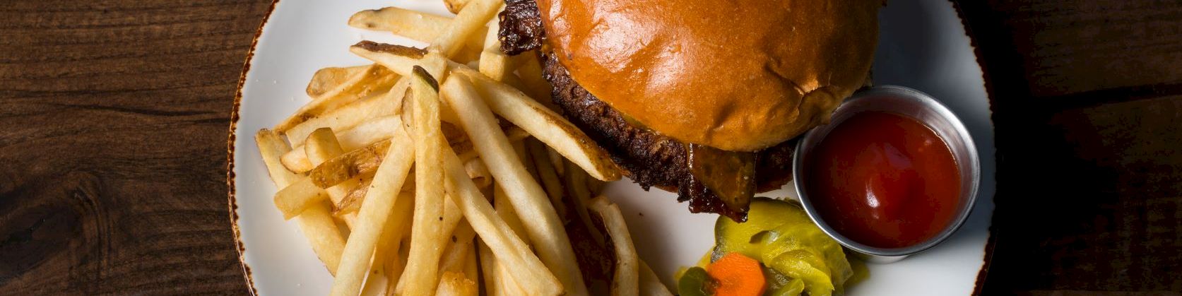 A plate with a burger, golden French fries, mixed veggies, and a small cup of ketchup sauce.