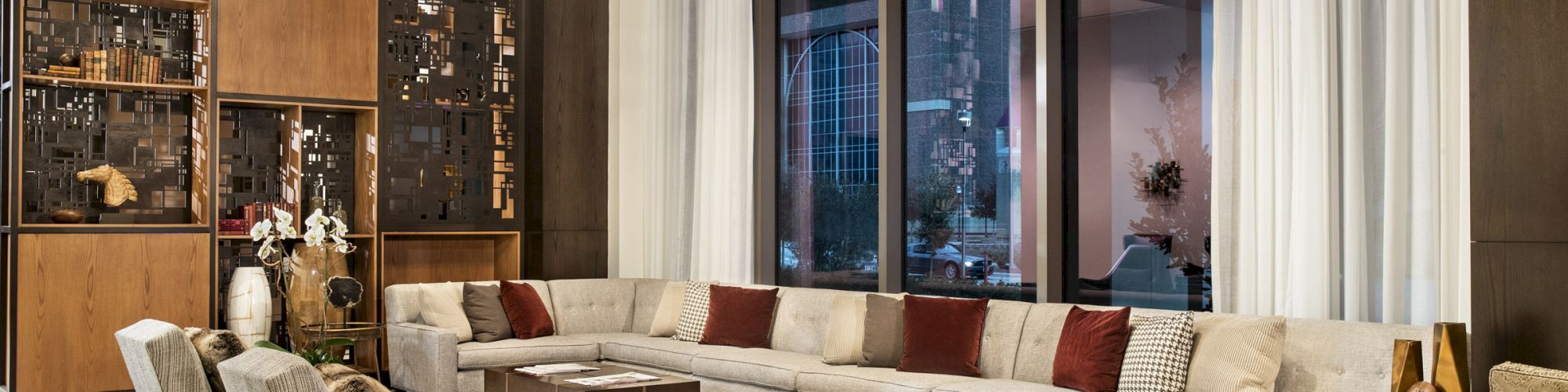 A modern, elegant living room features a large beige sectional sofa with red cushions, multiple coffee tables, and stylish chairs on a patterned rug.