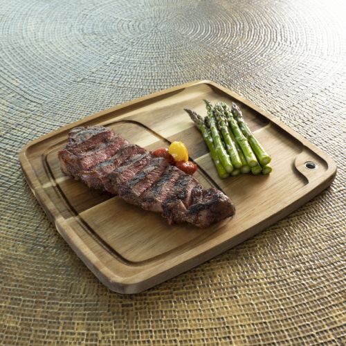 A sizzling steak on a wooden board with grilled asparagus, a lemon wedge, and a small dollop of sauce&mdash;rustic outdoor dining vibe.