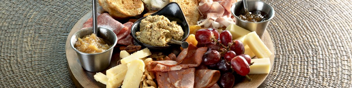 A charcuterie platter with cured meats, cheeses, grapes, bread, nuts, and spreads on a wooden board.