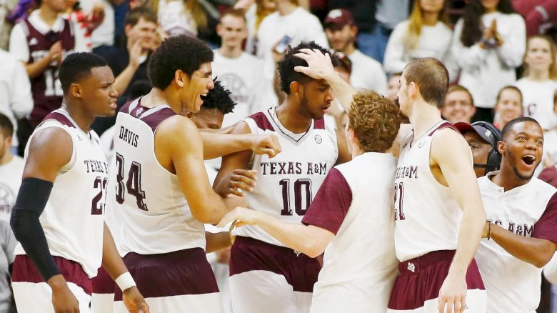 A group of Texas A&M basketball players are celebrating a victory on the court, with one player, number 10, in the center.