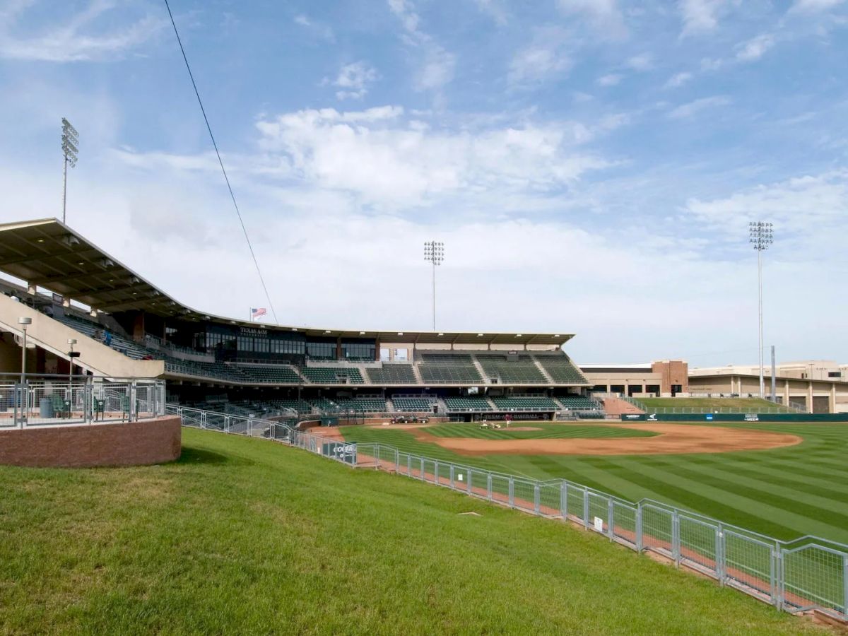 This image shows an empty baseball stadium with seating, light posts, a well-maintained field, and a partly cloudy sky in the background.
