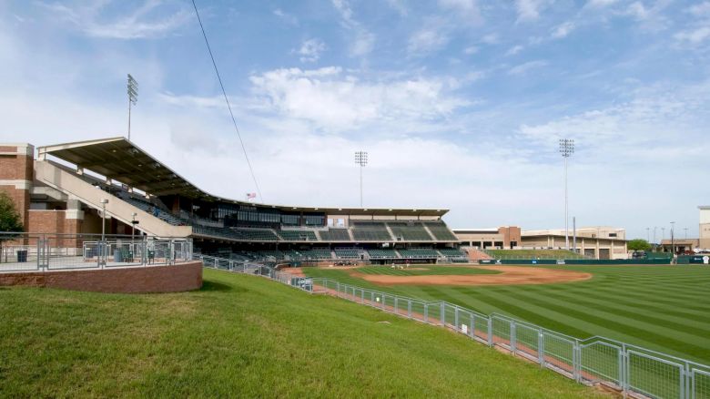 This image shows an empty baseball stadium with seating, light posts, a well-maintained field, and a partly cloudy sky in the background.