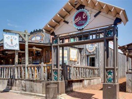 The image shows the exterior of a rustic wooden establishment called "Arlie L. Alley." The setting appears to be a western-themed location.