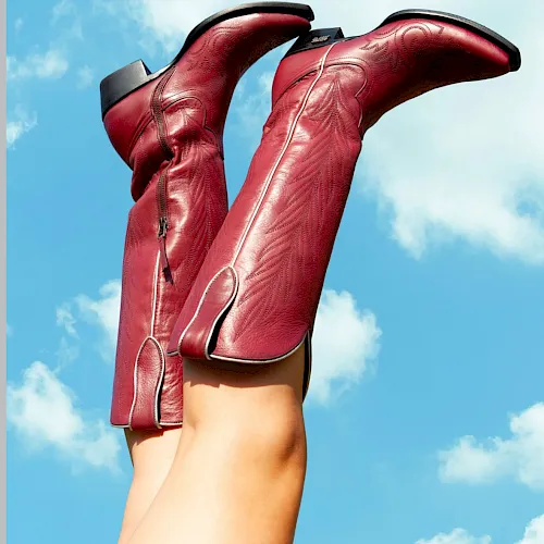 An Instagram post shows two red cowboy boots with white stitching held against a blue sky with clouds, by lane.official.