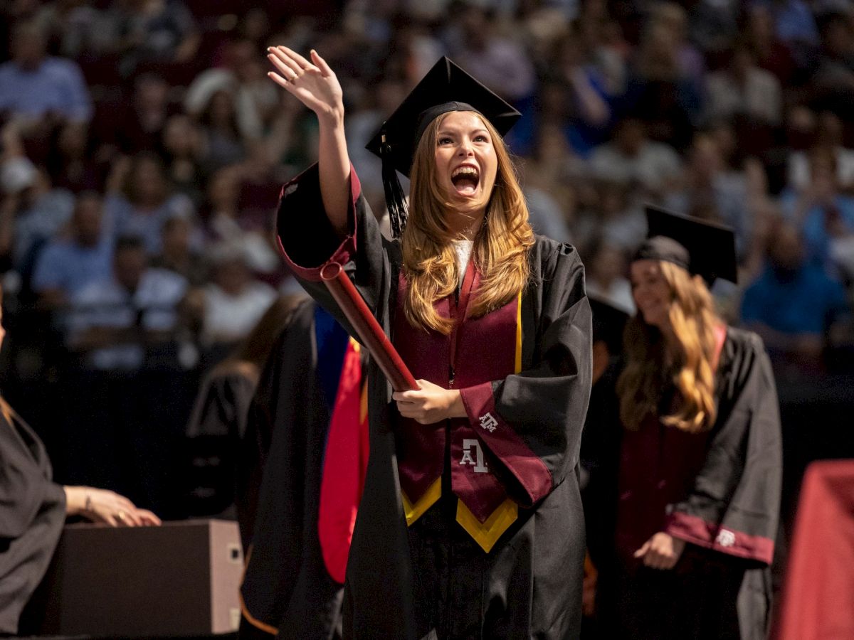 girl waving as she walks across the graduation stage