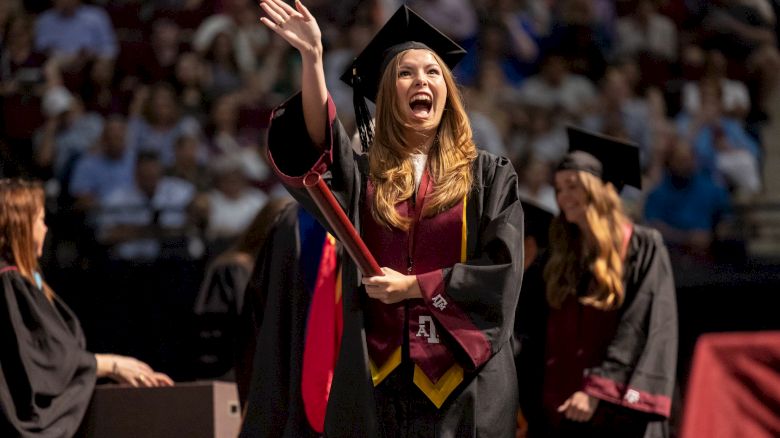 girl waving as she walks across the graduation stage