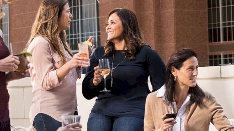 A group of people are socializing outdoors, holding drinks and engaging in conversation. They appear to be enjoying a casual, friendly gathering.