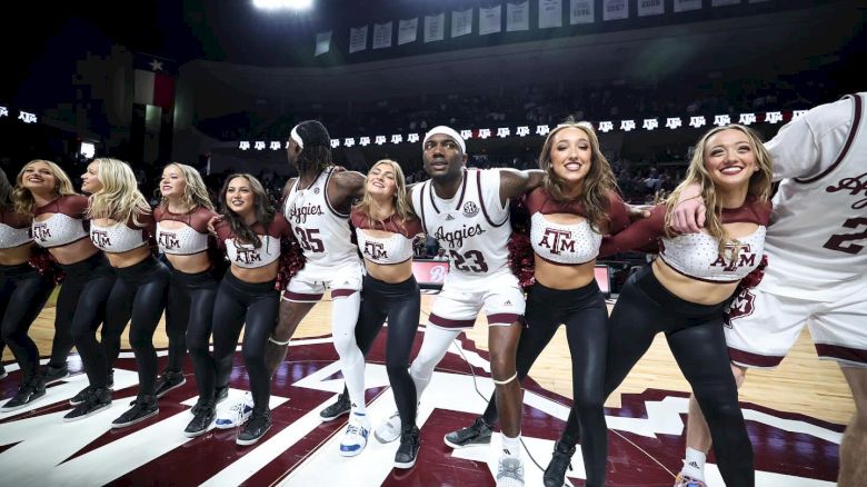 A group of cheerleaders and basketball players are standing on a court with arms linked, smiling and celebrating under bright lights.