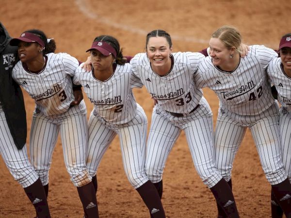 A group of softball players in striped uniforms, with arms around each other, on the field.