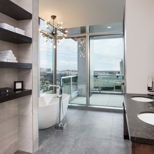 A modern bathroom features a double vanity, a freestanding tub, open shelving, and large windows with a balcony view.