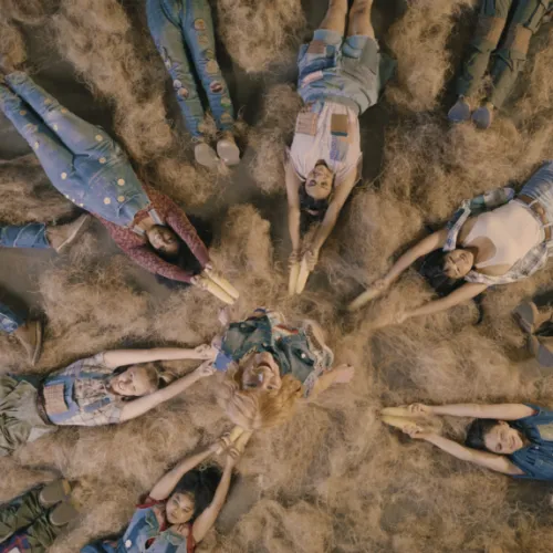 Top-down: people in denim and plaid lie together on dry grass, smiling in a circle.