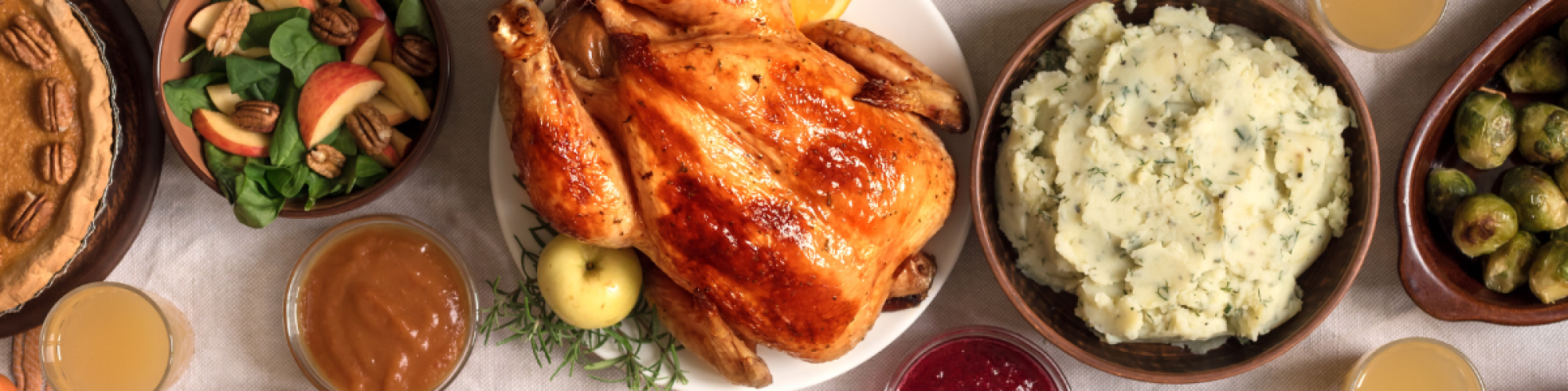 A festive table setting with a roasted turkey, mashed potatoes, various sides, drinks, and autumn decor such as leaves and pinecones, always ending the sentence.