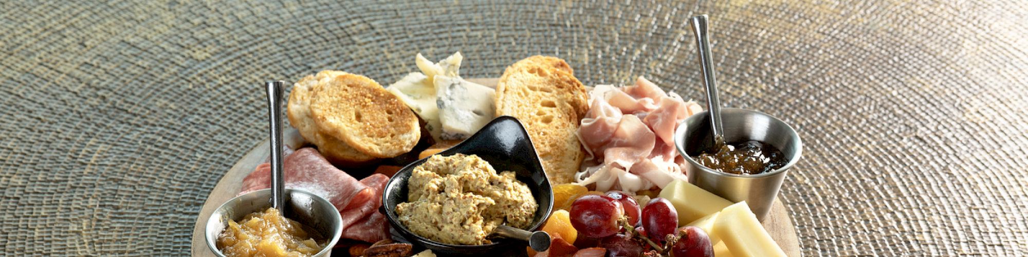 The image shows a charcuterie board with meats, cheeses, grapes, crackers, spreads, and nuts, arranged on a wooden platter.