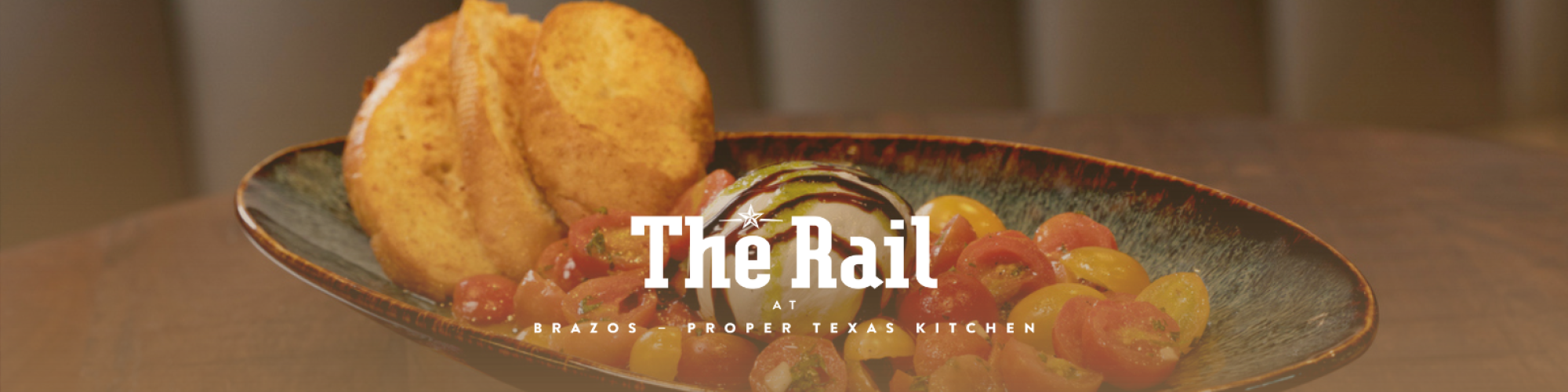 A dish with sliced tomatoes and an onion, garnished with toasted bread, and the text "The Rail" in front.