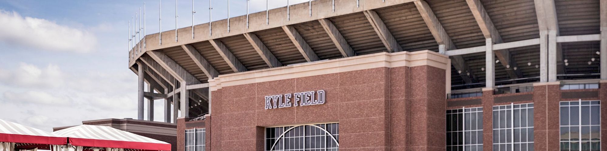 This image shows a swimming pool with lounge chairs, a cabana, and a large stadium named Kyle Field in the background.