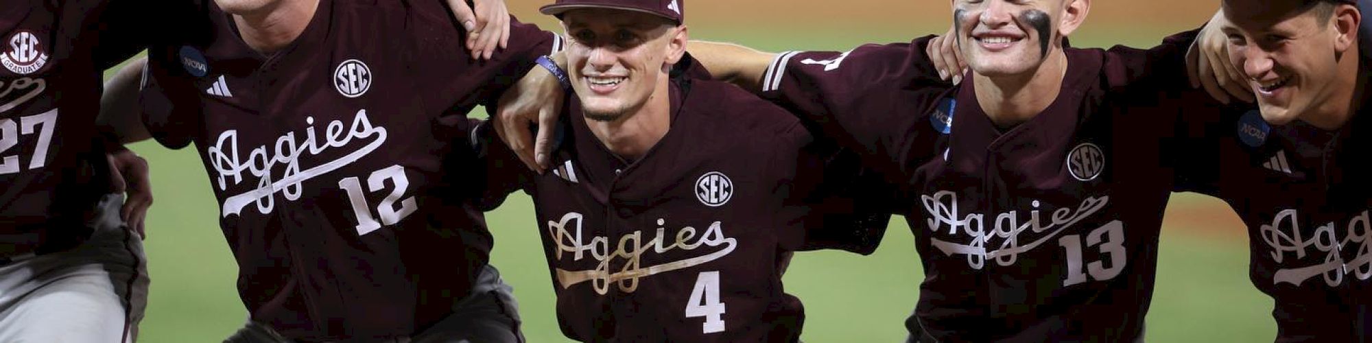 Five baseball players in maroon uniforms, labeled "Aggies," celebrate on the field with arms around each other, smiling and showing camaraderie.