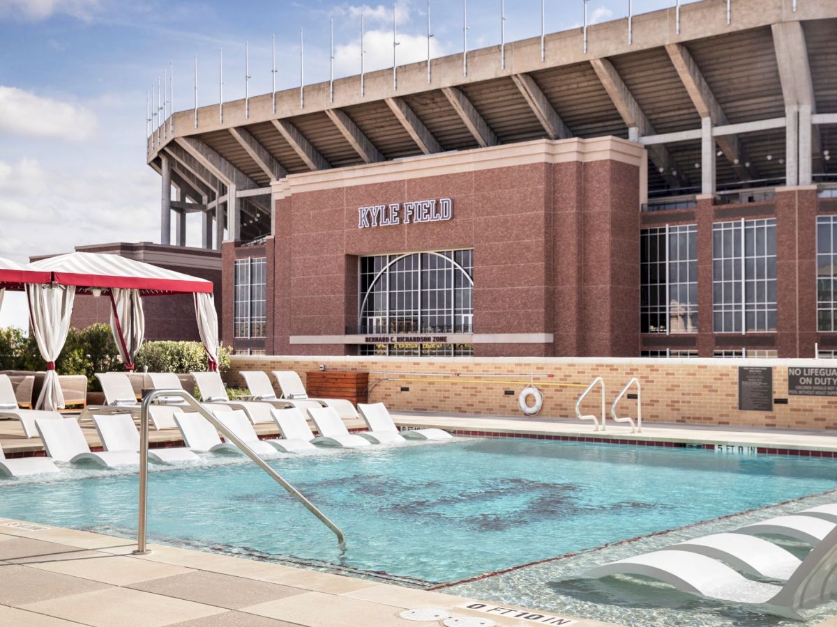 A swimming pool area with lounge chairs is in the foreground, and a large stadium structure labeled "Kyle Field" is visible in the background.