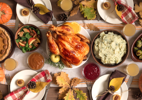 A festive Thanksgiving spread with a roast turkey at the center, surrounded by mashed potatoes, cranberry sauce, greens, pie, and drinks.