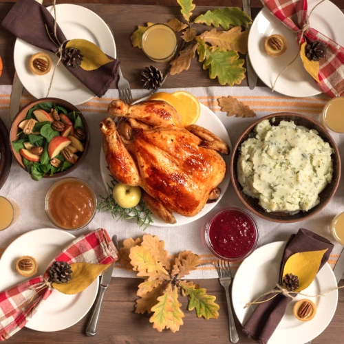 A festive Thanksgiving spread with a roast turkey at the center, surrounded by mashed potatoes, cranberry sauce, greens, pie, and drinks.