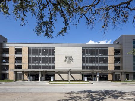 A parking garage with the Texas A&M University logo on the facade, surrounded by trees and a clear blue sky.