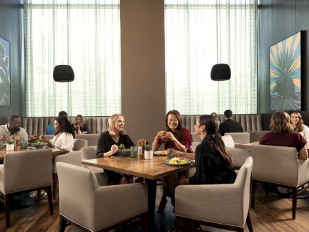 People dining in a modern restaurant with large paintings, soft lighting, and comfortable seating.