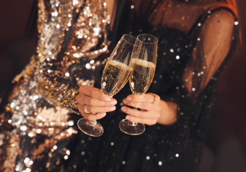 Two people in sparkly outfits clinking champagne glasses, celebrating or toasting an event or occasion.