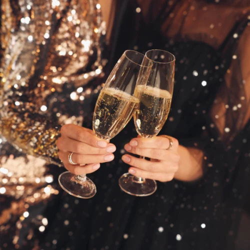 Two people in sparkly outfits clinking champagne glasses, celebrating or toasting an event or occasion.