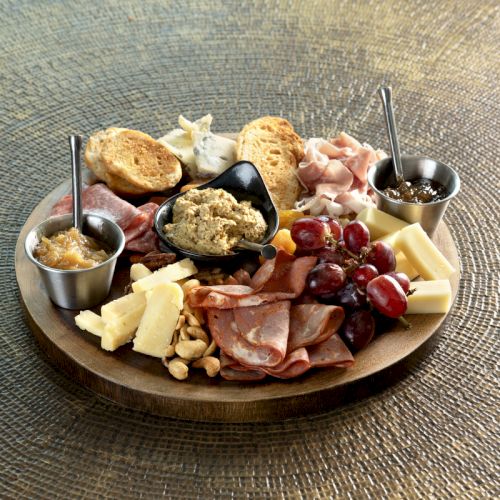 A charcuterie board with meats, cheeses, grapes, nuts, spreads, and bread arranged artfully on a round wooden platter.