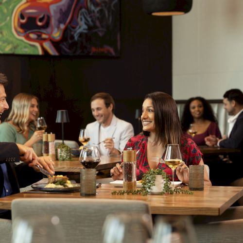 People dining in a restaurant, engaged in conversation, with wine and food on the tables, set in a modern, cozy ambiance.