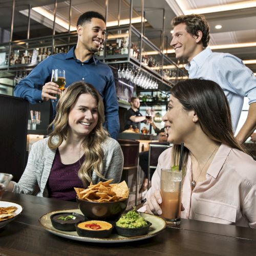 A group of friends is enjoying drinks and food at a restaurant, sharing smiles and conversations in a lively atmosphere.